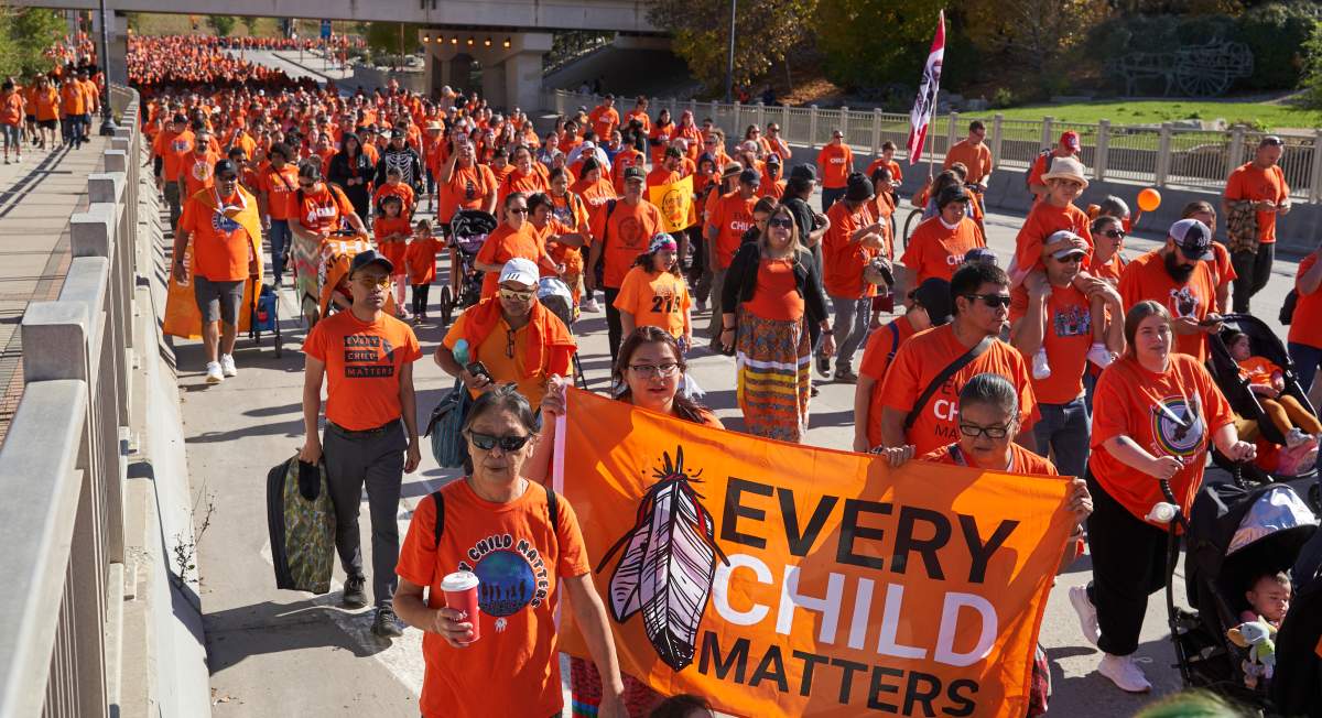 People participating in the Orange Shirt Day Survivors Walk pass the Canadian Museum for Human Rights in Winnipeg on Saturday, September 30, 2023.